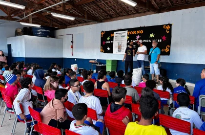 3 palestrantes, ao palco, com uma plateia de crianças atentas