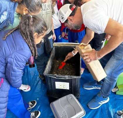 Palestrante manuseando uma caixa de compostagem com alunos à sua volta