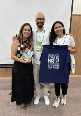 CEO da Preservalle, Rafael Guimarães, posando com mais duas participantes, expondo um livreto e uma camisa da Preservalle