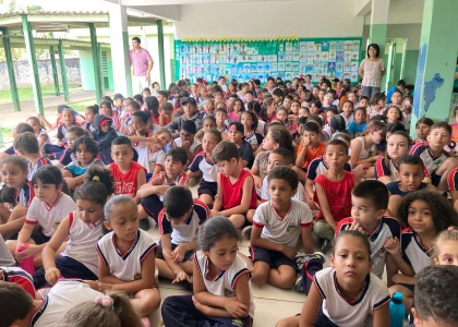 Crianças sentadas no pátio da escola atentas ao que está sendo ministrado